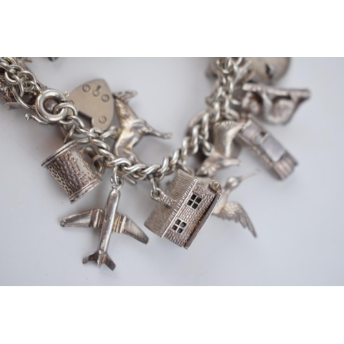 496 - Silver charm bracelet with a collection of charms to include London Bridge, a Bobby's helmet, a plan... 