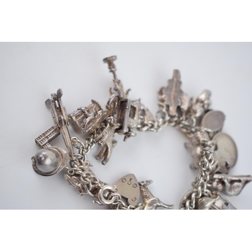 496 - Silver charm bracelet with a collection of charms to include London Bridge, a Bobby's helmet, a plan... 