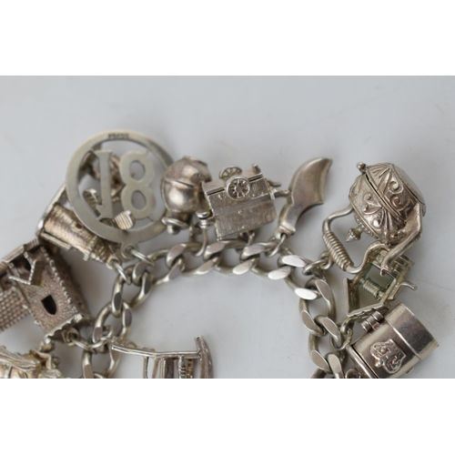 389 - Silver charm bracelet with charms to include a windmill, a bell, a teapot and others, 81.6 grams.