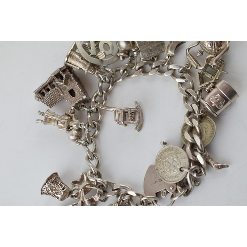 389 - Silver charm bracelet with charms to include a windmill, a bell, a teapot and others, 81.6 grams.