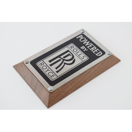 139 - An original 'Rolls-Royce' (Powered By) badge mounted on factory American black walnut. 15cm x 10cm x... 