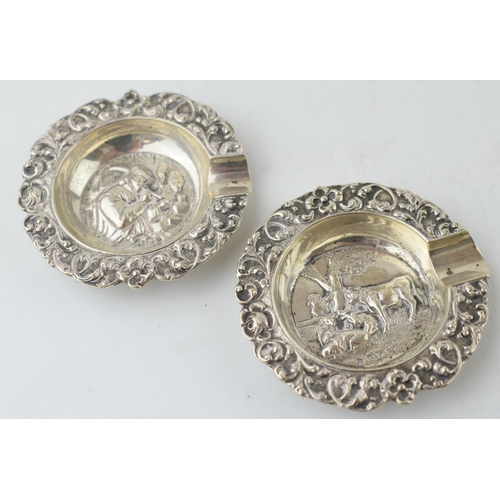 232 - A pair of sterling silver ashtrays with embossed scenes to include cows resting and a man dressed in... 