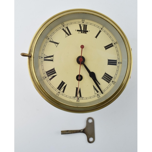 387 - A brass cased bulkhead clock with mechanical movement. Made in England, Cream dial with Roman Numera... 