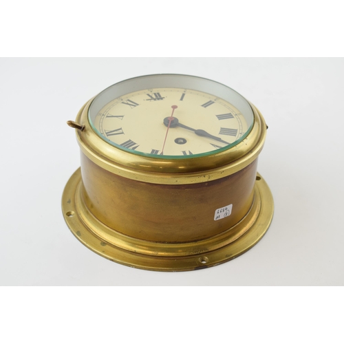 387 - A brass cased bulkhead clock with mechanical movement. Made in England, Cream dial with Roman Numera... 