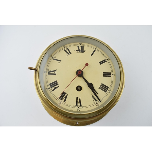 387 - A brass cased bulkhead clock with mechanical movement. Made in England, Cream dial with Roman Numera... 