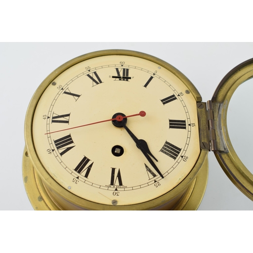 387 - A brass cased bulkhead clock with mechanical movement. Made in England, Cream dial with Roman Numera... 