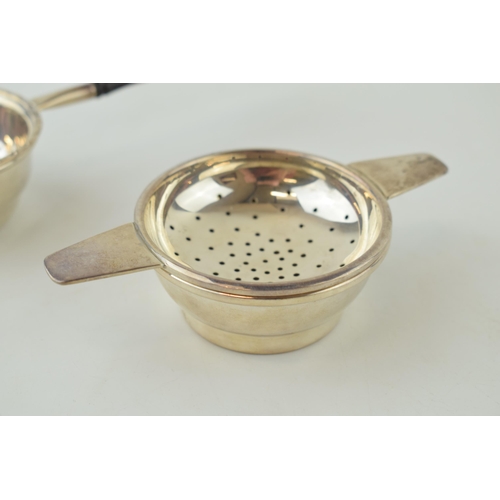 585 - Two silver tea strainers, 1 with a turned ebonised handle, London 1984, 17.5cm long, with a similar ... 