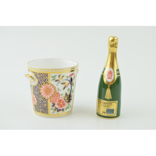 35 - A Royal Crown Derby miniature Champagne bottle together with a two handled cup. Height 9cm. (2)