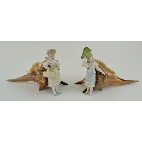 101 - A pair of late 19th / early 20th century pottery figures of children sat on elongated sea shells, un... 