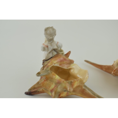 101 - A pair of late 19th / early 20th century pottery figures of children sat on elongated sea shells, un... 