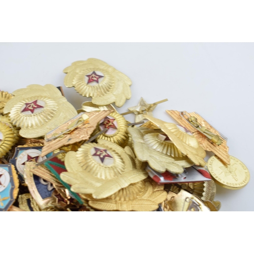 445 - A large collection of military cap badges and ribbons predominantly of Russian origin. (Qty)