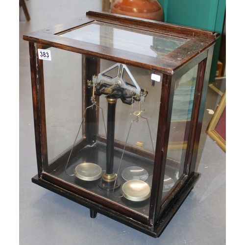 383 - Cased set of scientific weighing scales, indistinct maker, glass and wooden case, sliding door.