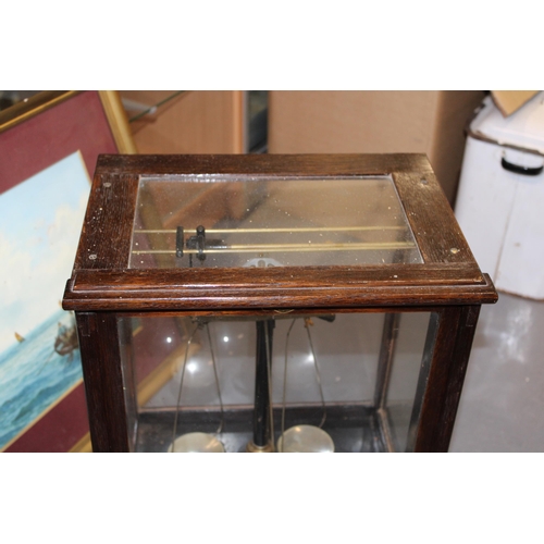 383 - Cased set of scientific weighing scales, indistinct maker, glass and wooden case, sliding door.