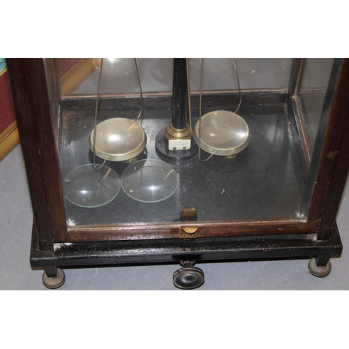 383 - Cased set of scientific weighing scales, indistinct maker, glass and wooden case, sliding door.