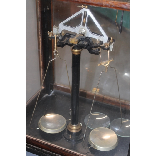 383 - Cased set of scientific weighing scales, indistinct maker, glass and wooden case, sliding door.