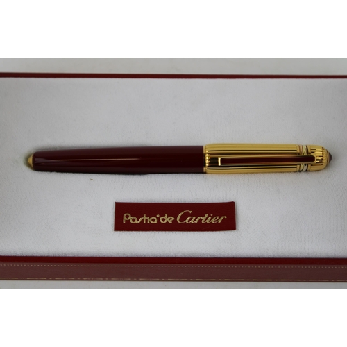 247 - Cartier, Pasha de Cartier, a roller ball pen, with gold plated ribbed cap, red cabochon and burgundy... 