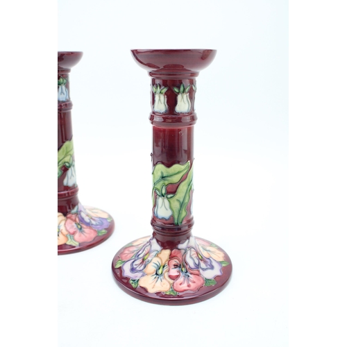 134 - A pair of Moorcroft candlesticks in the 'Pansy' pattern on Burgundy. Height 21cm.