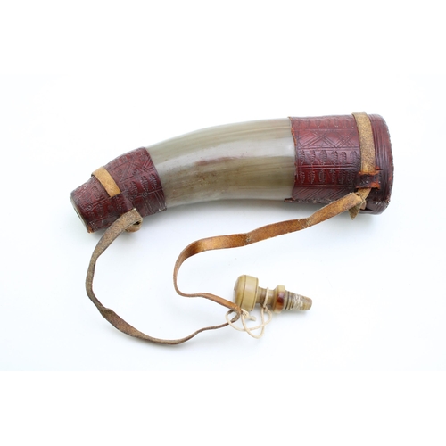 450 - An antique horn powder flask with turned horn stopper and shoulder strap with inscribed leather deco... 