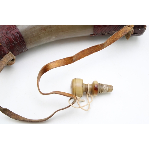 450 - An antique horn powder flask with turned horn stopper and shoulder strap with inscribed leather deco... 