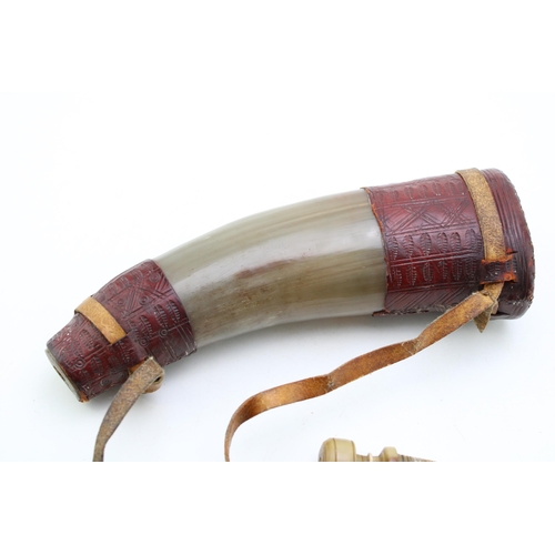 450 - An antique horn powder flask with turned horn stopper and shoulder strap with inscribed leather deco... 