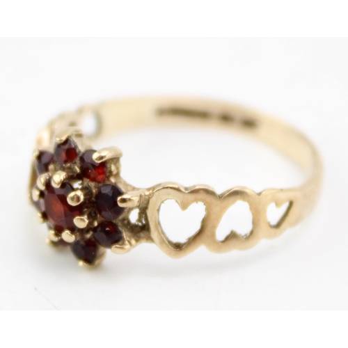 655 - A 9ct gold and garnet flowerhead ring with heart detailing to the shoulders, size Q/R, 2.0g