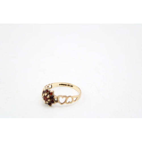 655 - A 9ct gold and garnet flowerhead ring with heart detailing to the shoulders, size Q/R, 2.0g