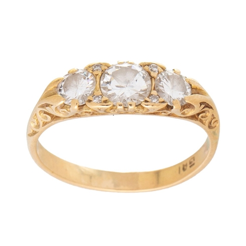 An 18ct gold and diamond three stone dress ring, the central stone of approximately 5.7mm diameter, 0.75ct, adjoined by two slightly smaller diamonds with four diamond brilliants surrounding central stone, all in scroll mount, size R/S, 4.3g.