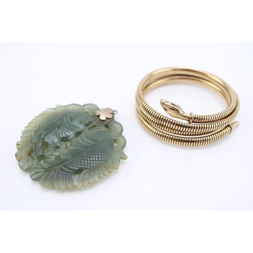 220 - A rolled gold serpent arm bangle and a spinach nephrite pendant carved as two fish, with silver flow... 