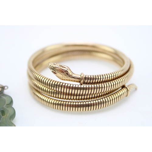 220 - A rolled gold serpent arm bangle and a spinach nephrite pendant carved as two fish, with silver flow... 