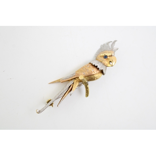 242 - A white and yellow gold brooch modelled as a cockatoo perched on a branch with sapphire eye, with te... 