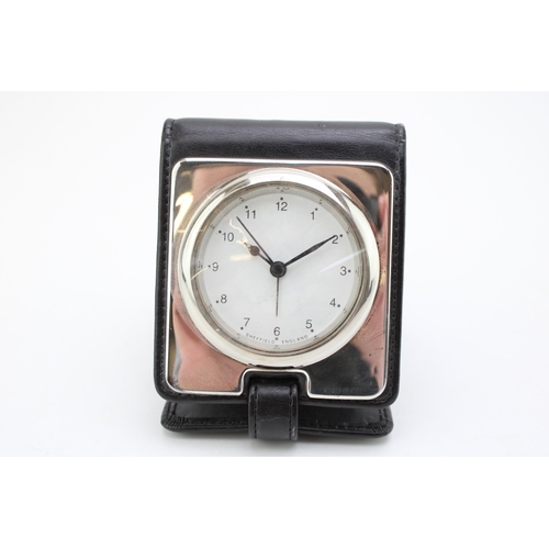 36 - A silver cased travel alarm clock, the white dial with Arabic numerals and minute track, in dark bro... 