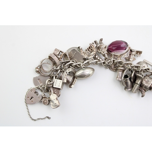 505 - A silver curb link charm bracelet with a large number of charms including a rugby ball, elephant, gr... 