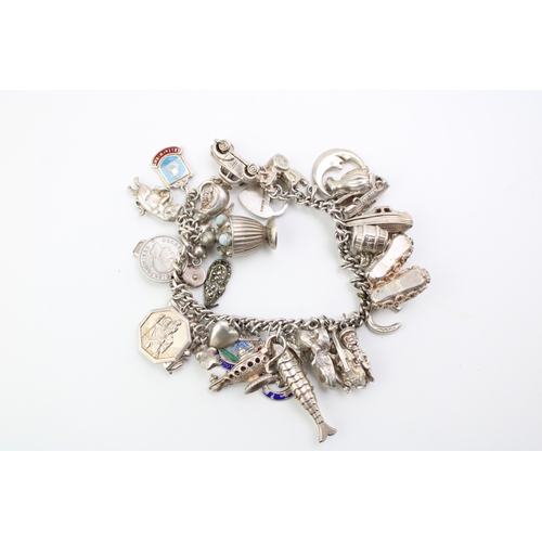 506 - A silver curb link charm bracelet with a large number of charms including a reticulated fish, motorb... 