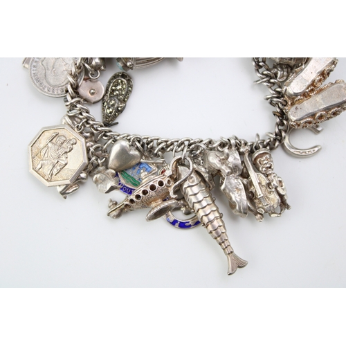 506 - A silver curb link charm bracelet with a large number of charms including a reticulated fish, motorb... 