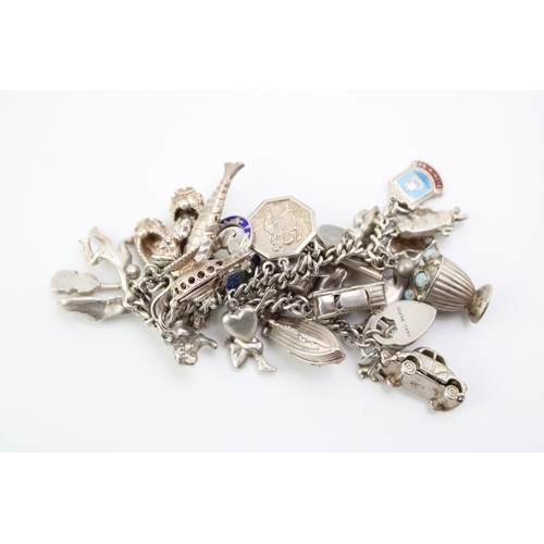 506 - A silver curb link charm bracelet with a large number of charms including a reticulated fish, motorb... 