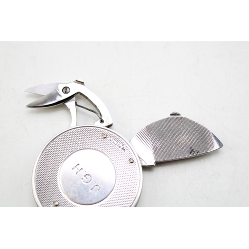163 - A silver circular fob with integral steel folding manicure set, comprising scissors, file and knife,... 