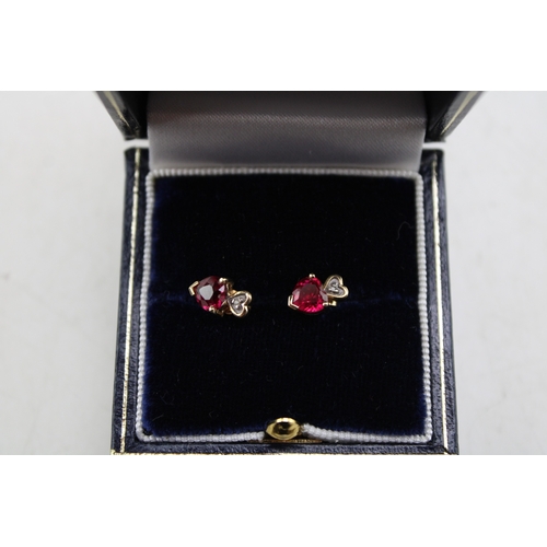 225 - A pair of 9ct gold, ruby and diamond earrings, set with heart cut rubies bellow a small diamond chip... 