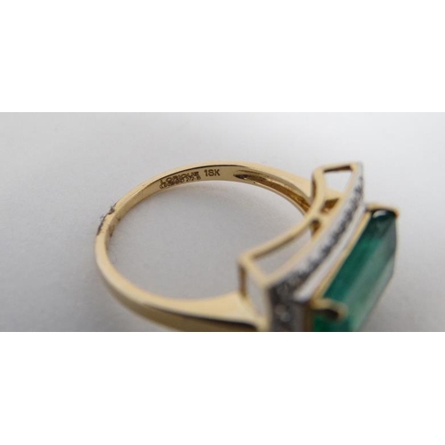 1012 - An 18ct gold ring set with central emerald bordered by diamonds.