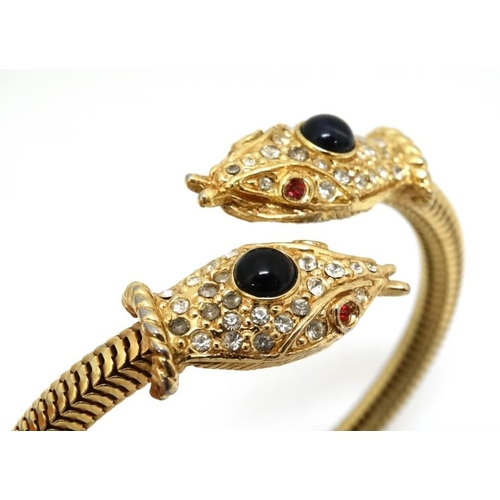 1047 - A gilt metal bracelet of bangle form the ends terminating in snake head decoration