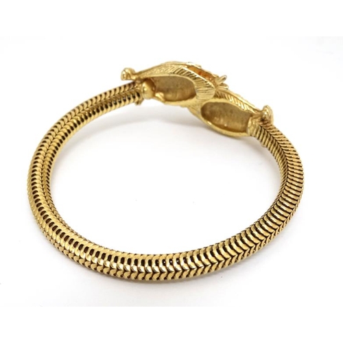 1047 - A gilt metal bracelet of bangle form the ends terminating in snake head decoration