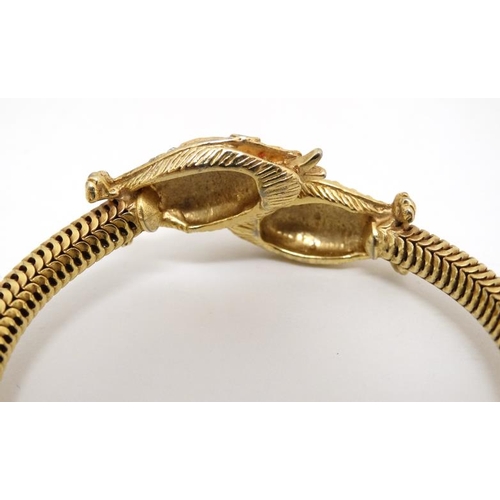 1047 - A gilt metal bracelet of bangle form the ends terminating in snake head decoration