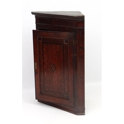 214 - A Georgian Oak hanging corner cupboard  with single panelled inlaid and crossbanded door opening to ... 