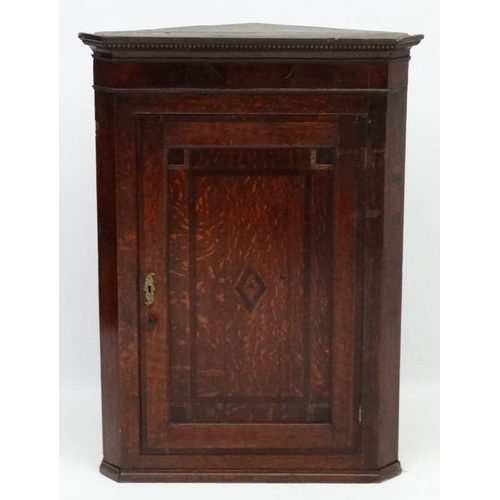 214 - A Georgian Oak hanging corner cupboard  with single panelled inlaid and crossbanded door opening to ... 