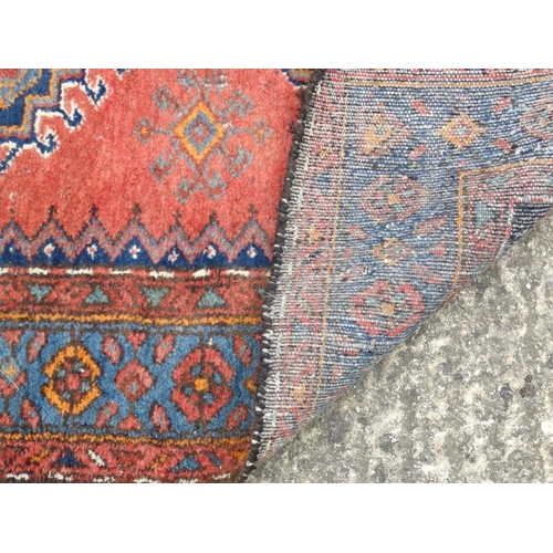 54 - Carpet / Rug : A woollen rug with blue and red/pink ground with geometric arrow like motifs 81'' x 4... 