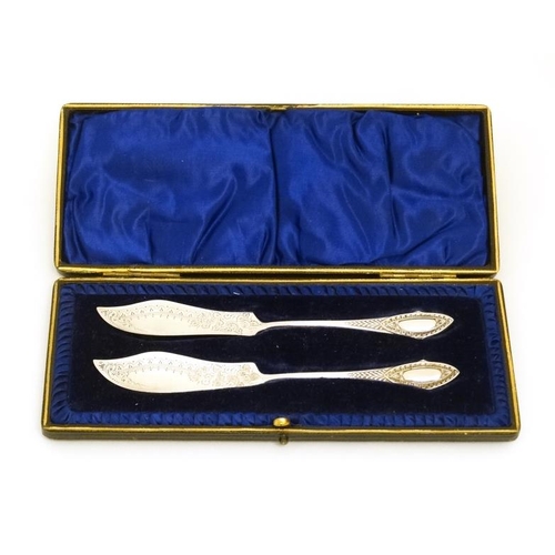 611 - A cased pair of silver plated butter knives with engraved decoration 5 3/4'' long