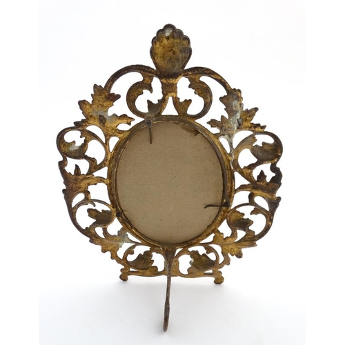 887 - A 19thC gilt metal strut / easel back frame with provision for oval, bordered by gilded  cast iron a... 