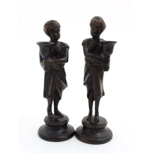 952 - A pair of cast bronze candlesticks in the form of eastern figures wearing a turban on a circular soc... 