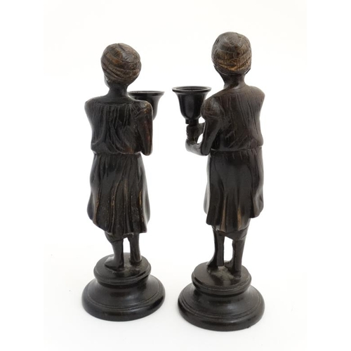 952 - A pair of cast bronze candlesticks in the form of eastern figures wearing a turban on a circular soc... 