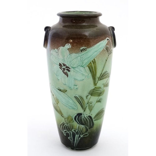 574 - A Moorcroft style twin handled vase decorated with tube lined trumpet flowers in shades of green on ... 