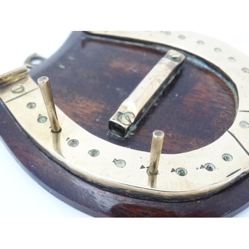 389 - A small brass cribbage board formed as a horseshoe, with two pegs and mounted upon a wooden plinth. ... 